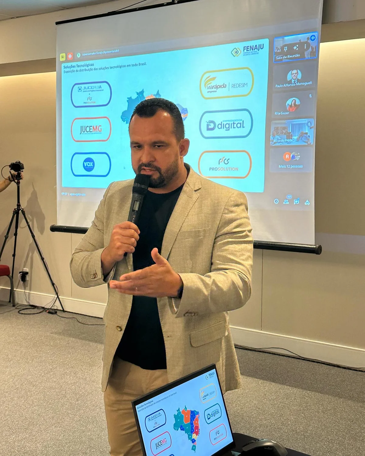 Aiuá Reis, de blazer bege, fala ao microfone diante de uma apresentação sobre soluções tecnológicas.