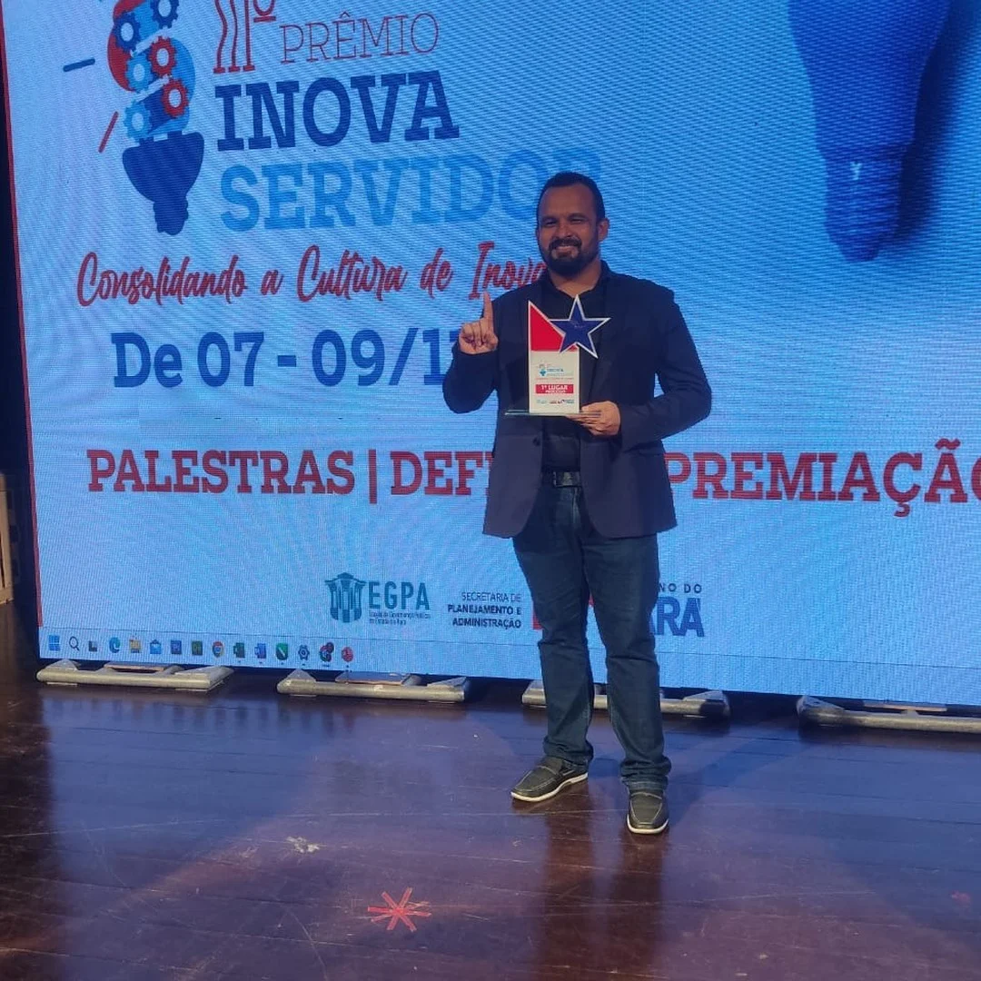 Aiuá Reis segura o troféu diante do painel do III Prêmio Inova Servidor.